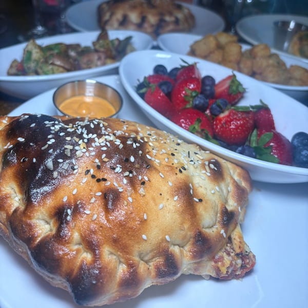Calzone with sesame seeds, dipping sauce, and bowls of fruit and other dishes on a table.