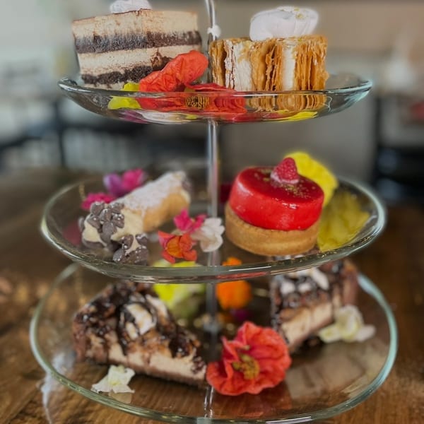 A three-tiered dessert stand filled with various pastries, including cakes, cannolis, and tarts, adorned with flowers.