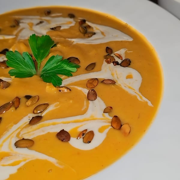 Close-up of Tarantino's Vegan pumpkin soup with cream swirls, pumpkin seeds, and parsley garnish.