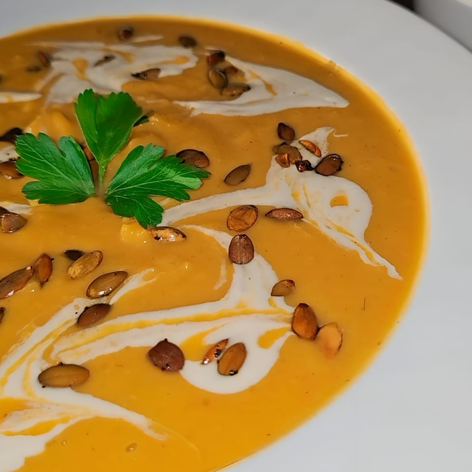 Close-up of Tarantino's Vegan pumpkin soup with cream swirls, pumpkin seeds, and parsley garnish.