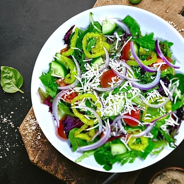 Vegan salad with mixed greens, red onion, bell peppers, tomatoes, cucumber, and shredded vegan cheese.