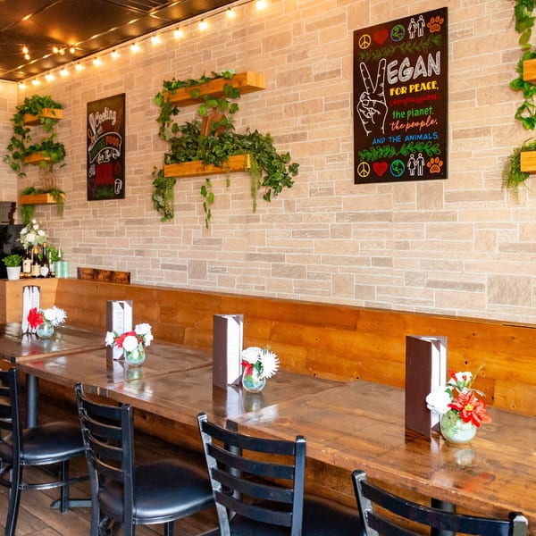 Interior of Tarantino's Vegan with long wooden tables, black chairs, and vegan-themed wall art.