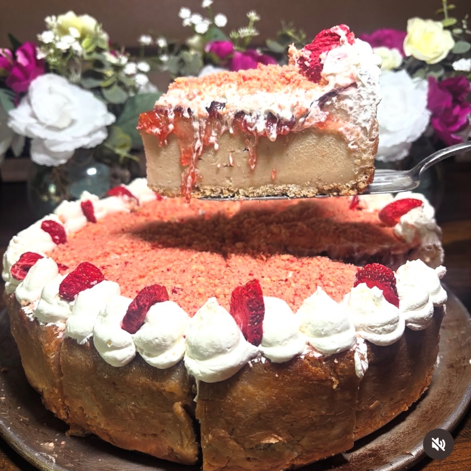Layered chocolate cake topped with pink frosting, whipped cream, and dried rose petals, with a fork lifting a slice.