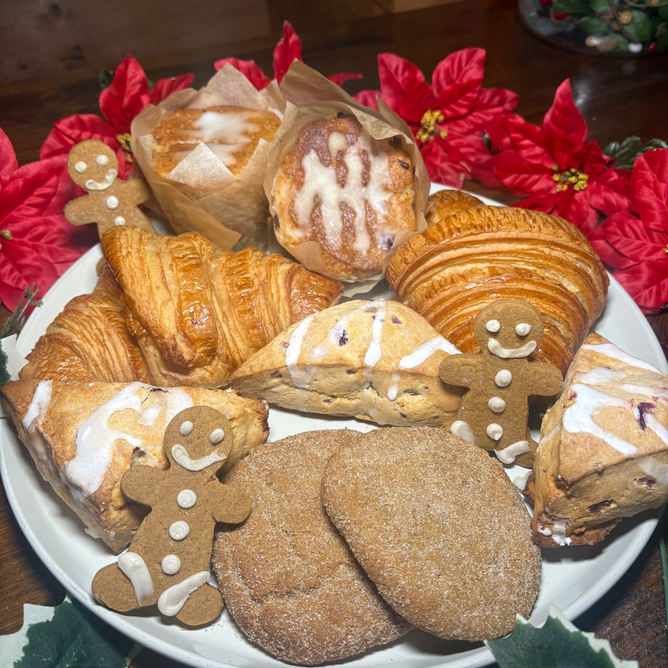 Festive platter of croissants, iced pastries, scones, gingerbread cookies, and gingerbread people surrounded by red poinsettias.