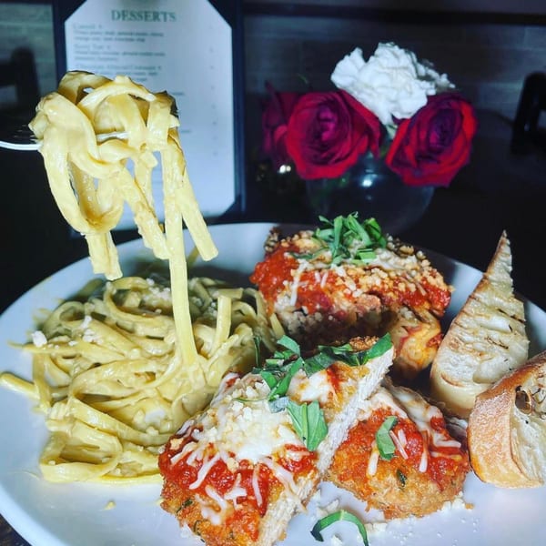 Vegan fettuccine alfredo and chicken parmesan with garlic bread, and red roses in the background.