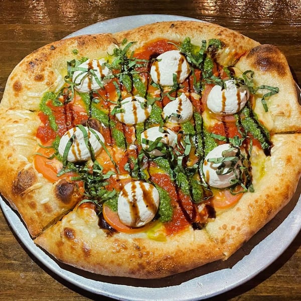 Vegan pizza with tomato, pesto, vegan mozzarella, basil, and balsamic glaze on a metal tray.