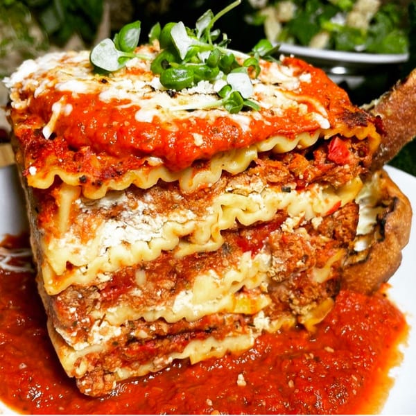 A large, layered vegan lasagna with rich red sauce, white cheese, and green garnish.
