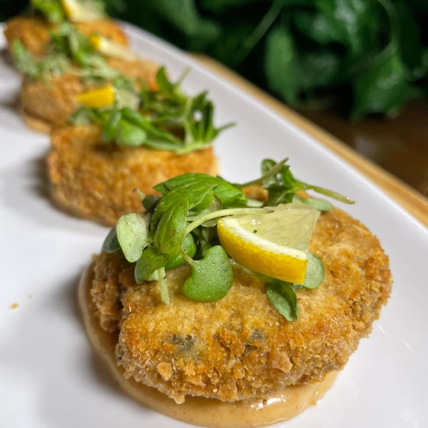 Three vegan crab cakes on a white plate, garnished with microgreens and lemon wedges.