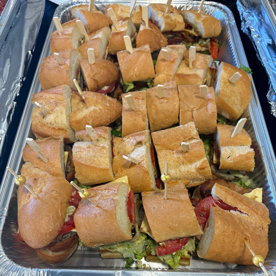 Assorted bite-sized sandwiches with lettuce, tomato, cheese, and deli meats arranged in a foil catering tray with picks.