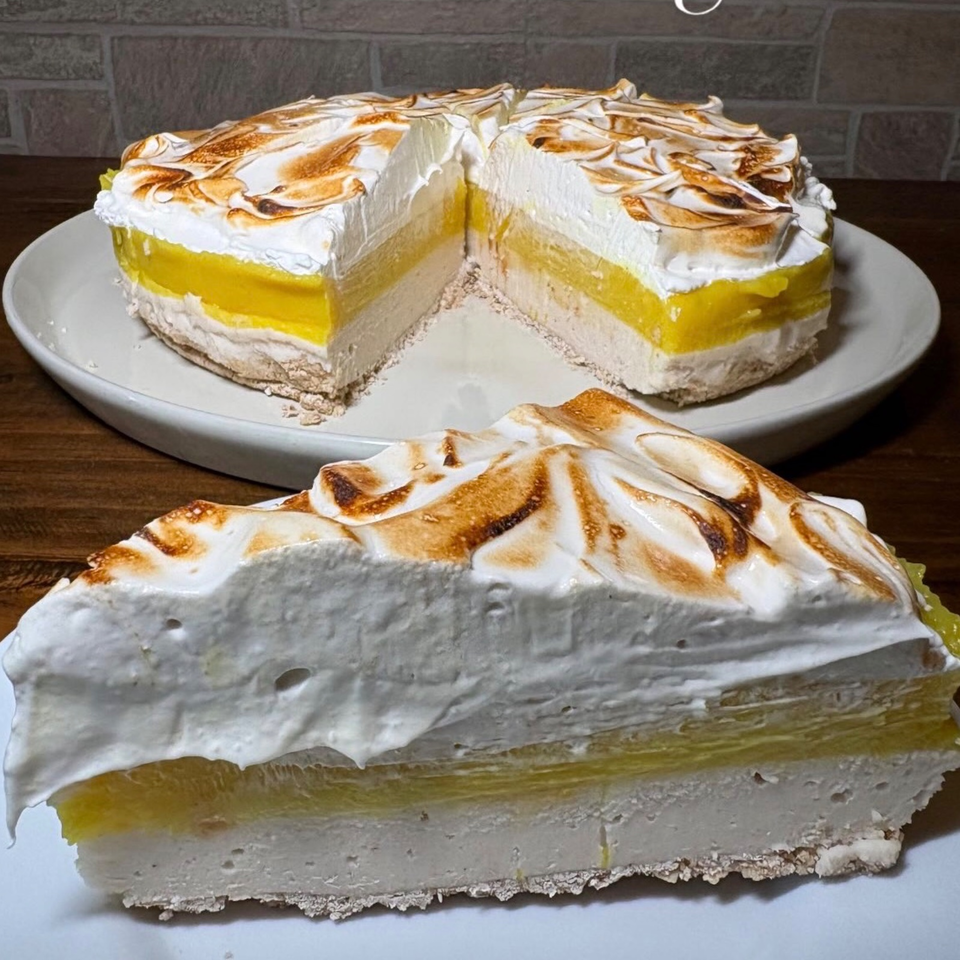 Slice of lemon meringue pie with toasted meringue, alongside a round pie on white plates.