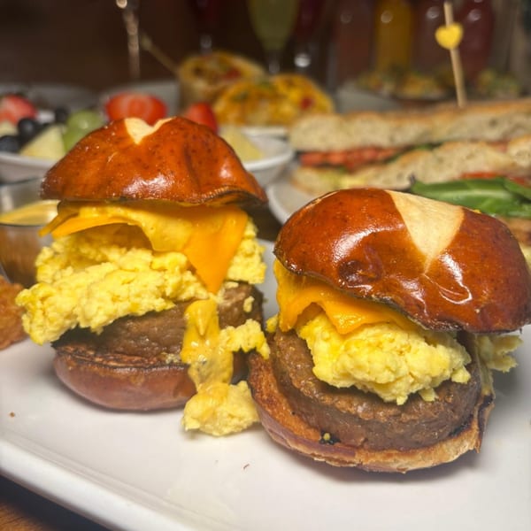 Two breakfast sliders with sausage, scrambled eggs, and cheese on pretzel buns.