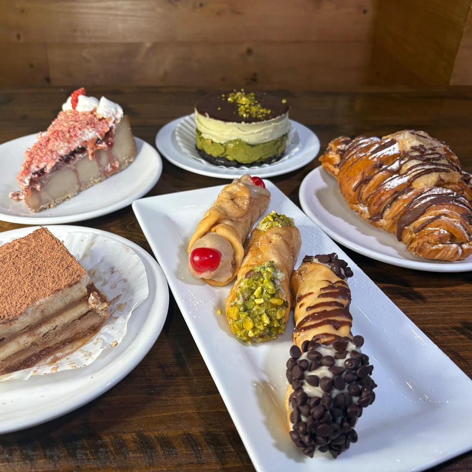 Assortment of decorated pastries and cakes on white plates atop a rustic wooden table.