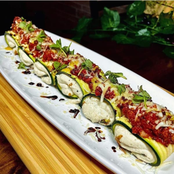 Vegan zucchini rolls filled with ricotta, topped with marinara, vegan parmesan, and fresh herbs.