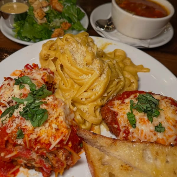 Vegan lasagna, fettuccine alfredo, chicken parmesan, garlic bread, salad, and soup on a table.