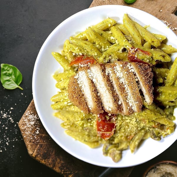 Vegan pesto penne pasta with breaded cutlets, cherry tomatoes, and grated vegan parmesan.