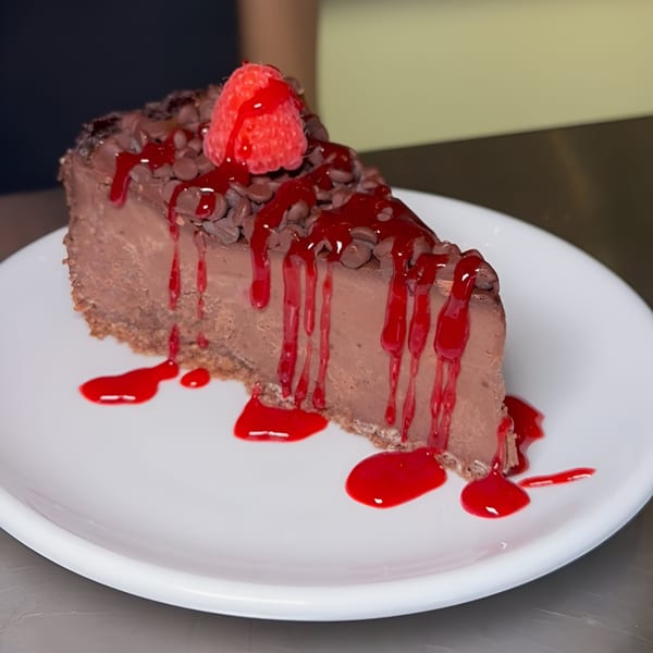 A slice of vegan chocolate cheesecake with raspberry drizzle and a whole raspberry on top.