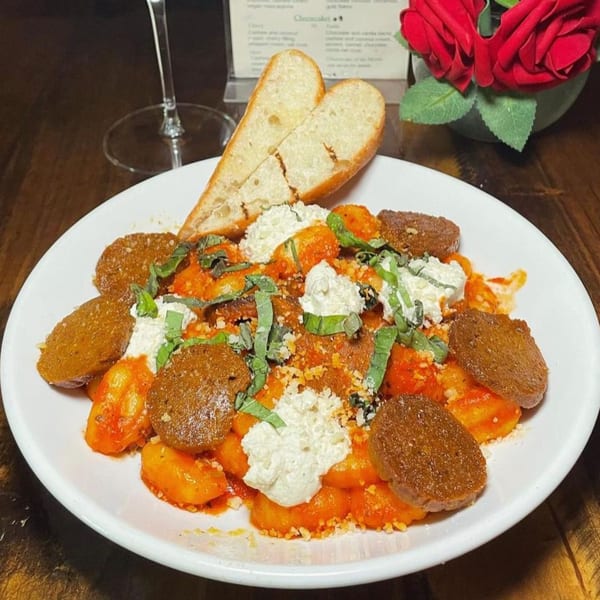 Vegan gnocchi with red sauce, vegan ricotta, basil, and sausage slices, served with heart-shaped bread.