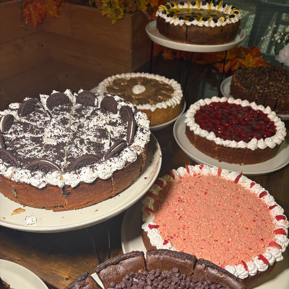 Assortment of decorated cakes, including chocolate cookie, berry, pink crumb, fruit-topped, and chocolate chip varieties, displayed on plates.