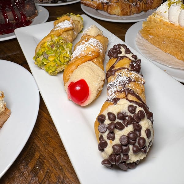 Three cannolis, one with pistachios, one with a cherry, and one with chocolate chips, on a white plate.